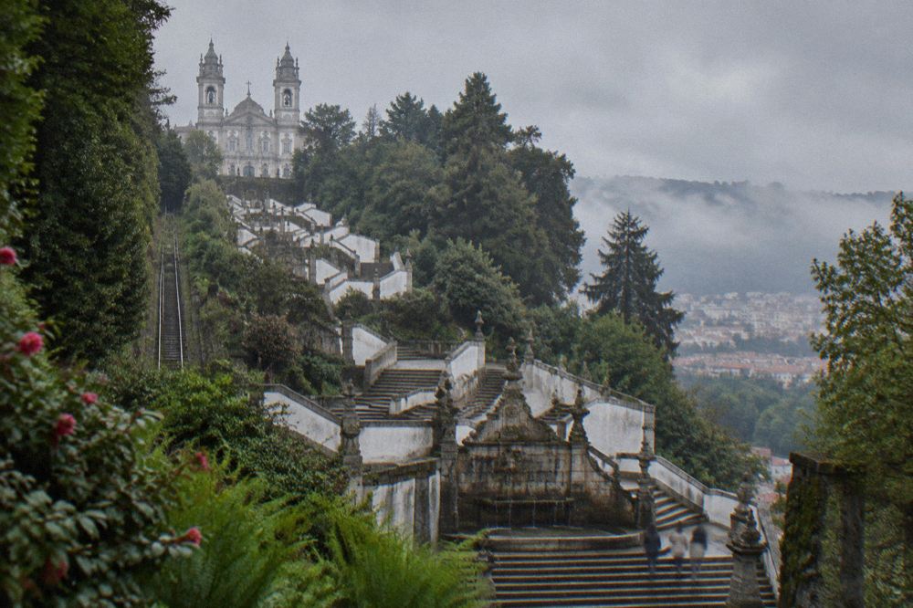 Stone steps and ornamental fountains on one landing of the Escadório, with the wooded slope and city rooftops beyond