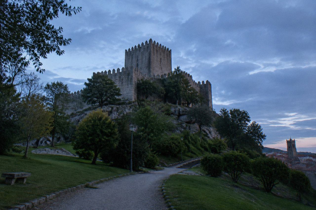 A stone palace tower rising above a medieval European town square with cobbled lanes and old roofs