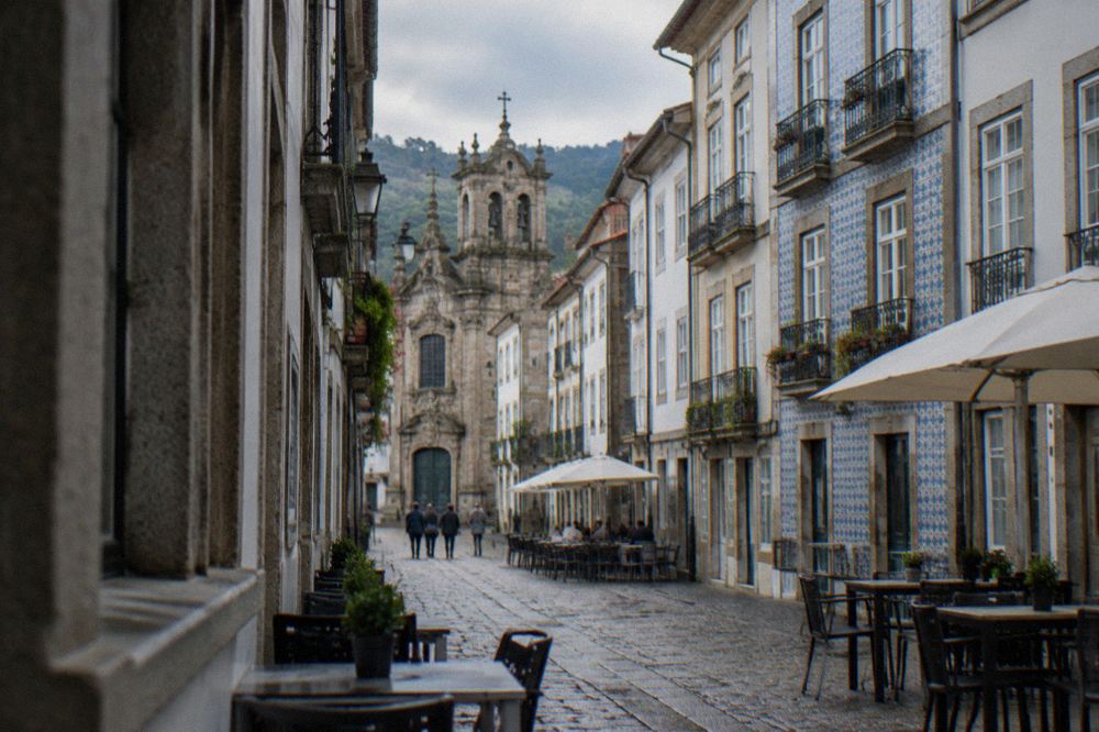 A narrow cobbled street in a Portuguese old town lined with granite buildings and cafe tables