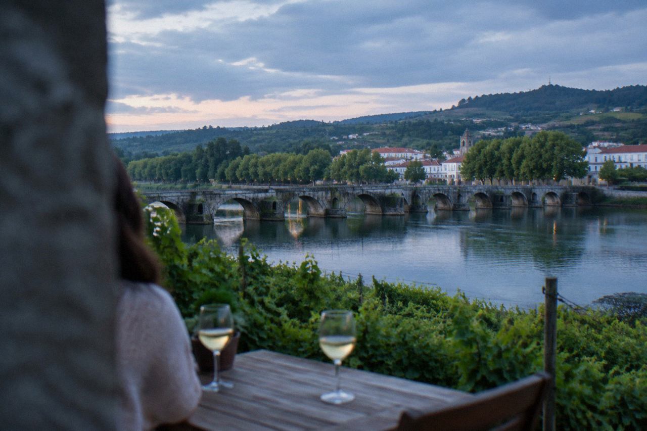 Two glasses of pale white wine on a wooden table beside a vineyard hillside