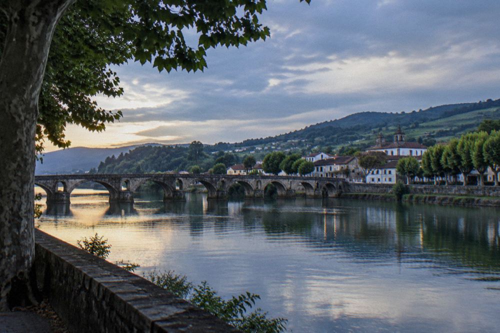 Medieval stone bridge over a calm river with a small historic town on the bank