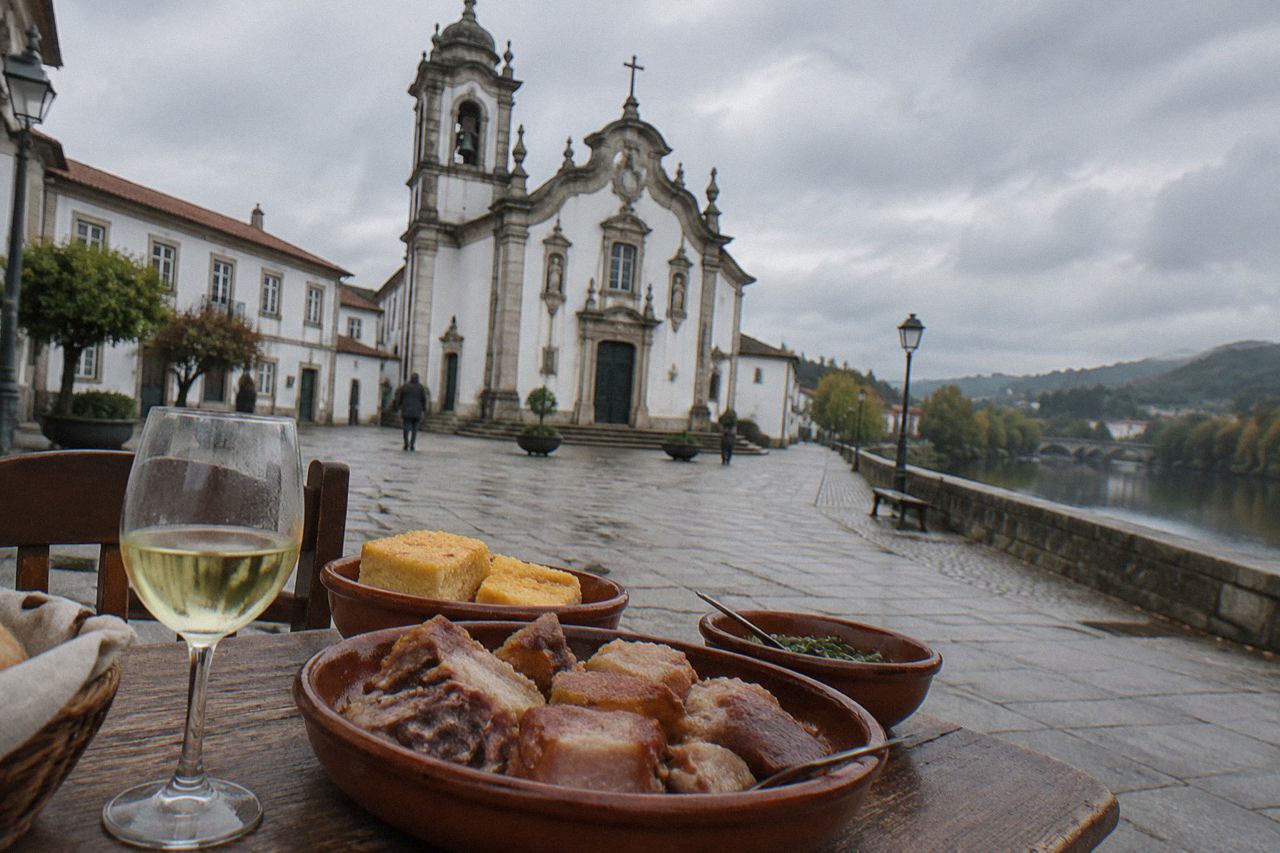 A rustic Minho table with clay dishes of pork meat, cornbread and a glass of young white wine