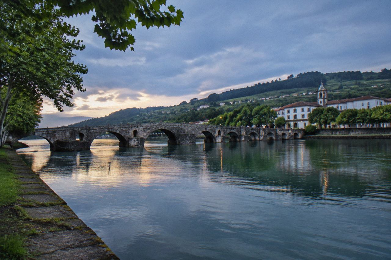A stone bridge crossing a wide green river with a small town on the far bank
