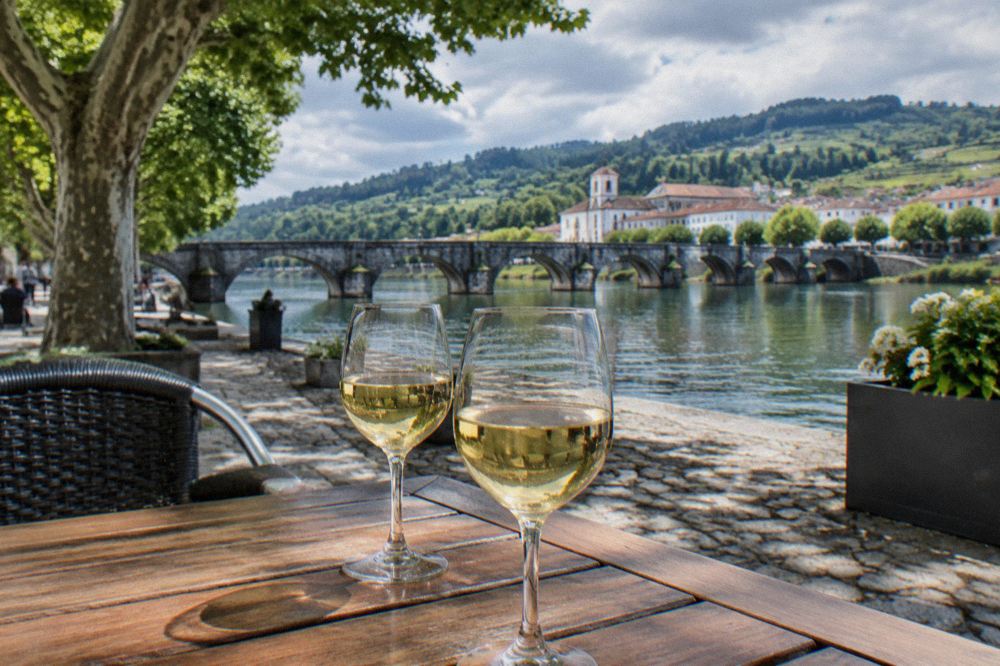 Two glasses of pale white wine with a faint sparkle, standing on a wooden café table in a Portuguese square