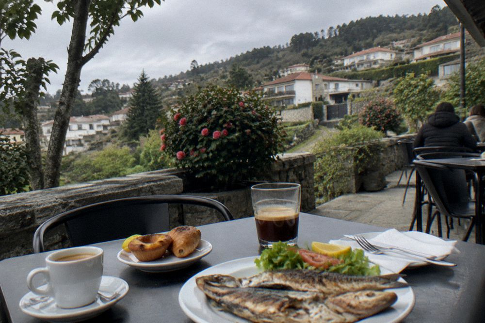 A table with coffee, pastries and a plate of grilled fish at a simple Portuguese café