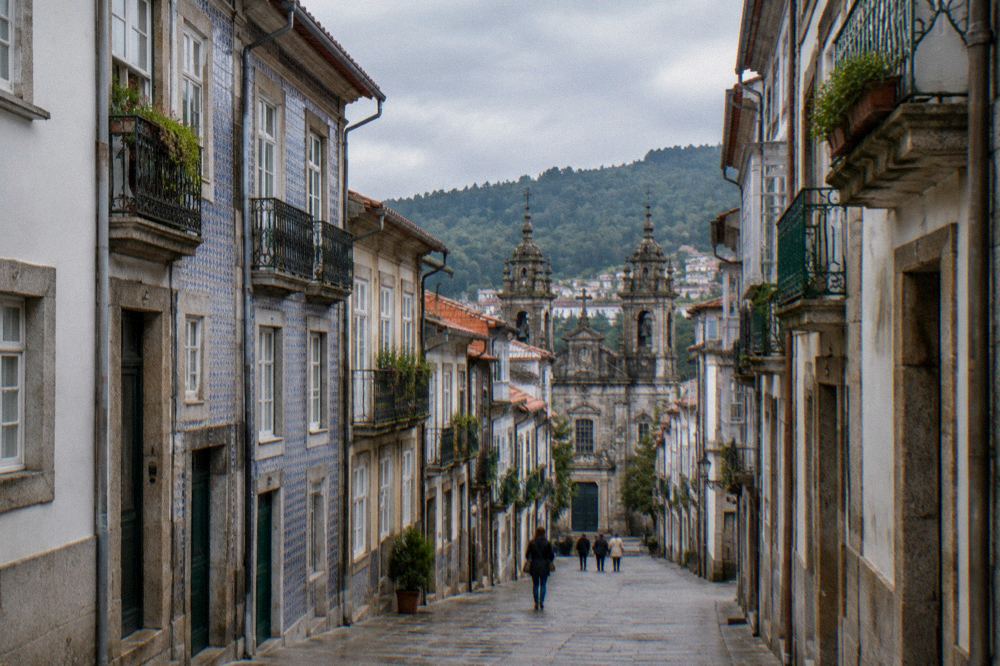 A narrow pedestrian street in Braga's old town with stone buildings leading downhill towards the cathedral towers