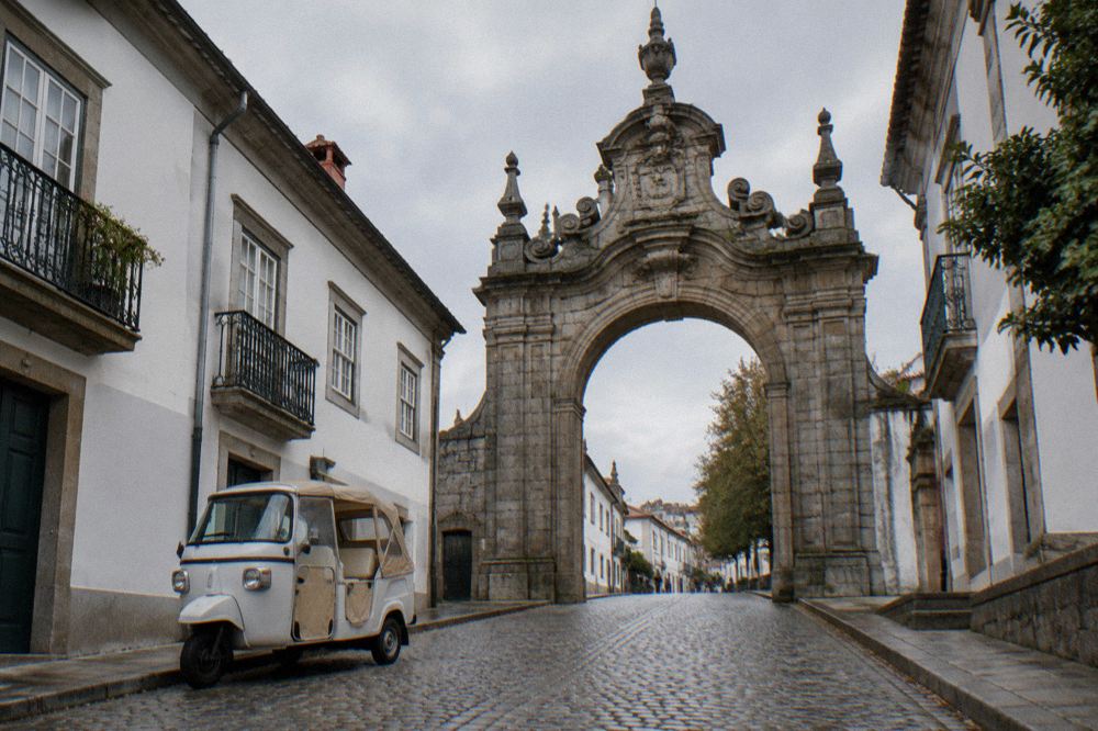 A small three-wheeled tuk tuk vehicle parked on a cobbled street near the old city gate in Braga