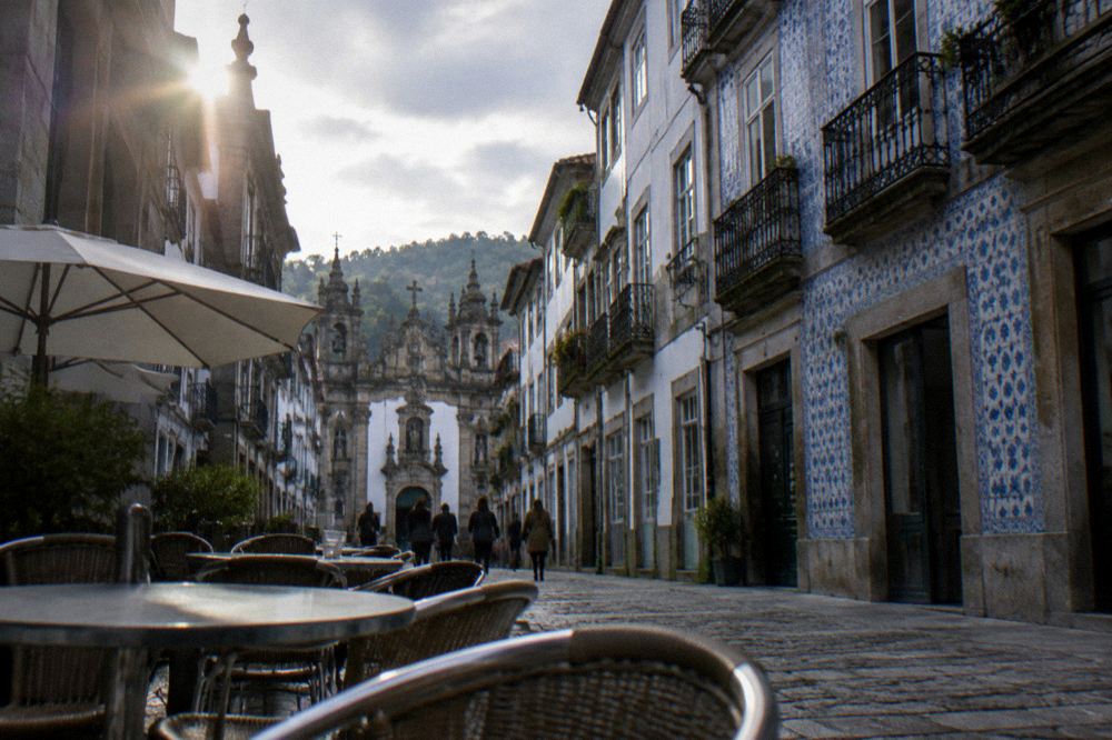 Café tables and chairs set out on a cobbled pedestrian street in Braga's old town near the stone arch