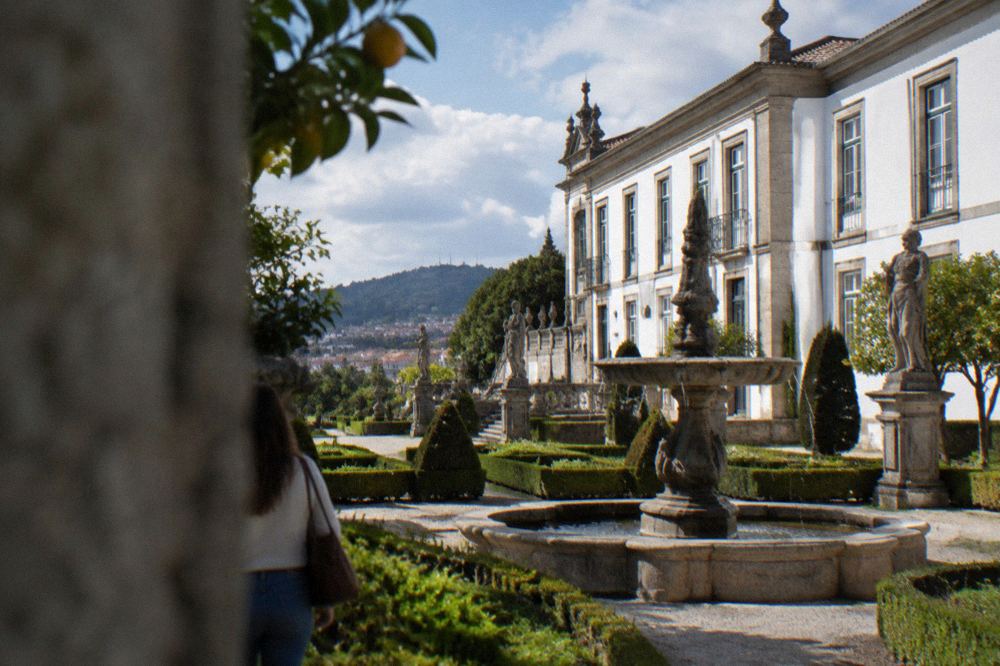 A formal garden with clipped hedges, a stone fountain and statuary beside the palace