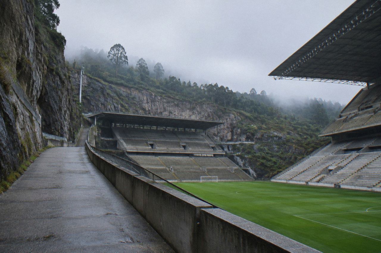 A large football stadium carved into a rock wall, with green pitch and empty concrete stands