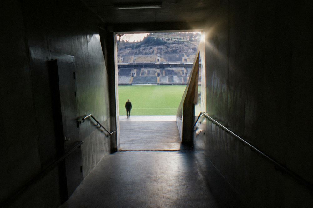 A tunnel corridor leading from a dressing room toward a bright football pitch