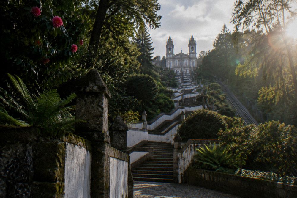 A baroque granite stairway zigzagging up a wooded hillside toward a church facade