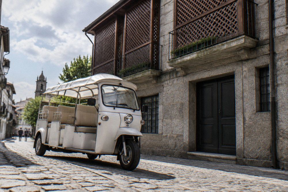 An electric tuk tuk vehicle parked on a cobbled street in a Portuguese city