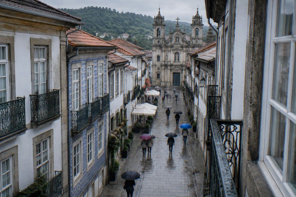 Visitors walking with umbrellas on a wet historic street in Braga
