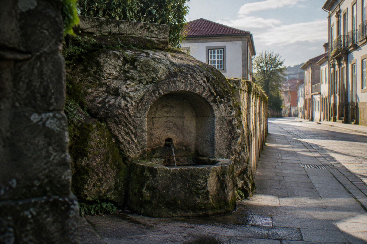 A granite rock face carved with a Roman fountain niche standing beside a quiet street