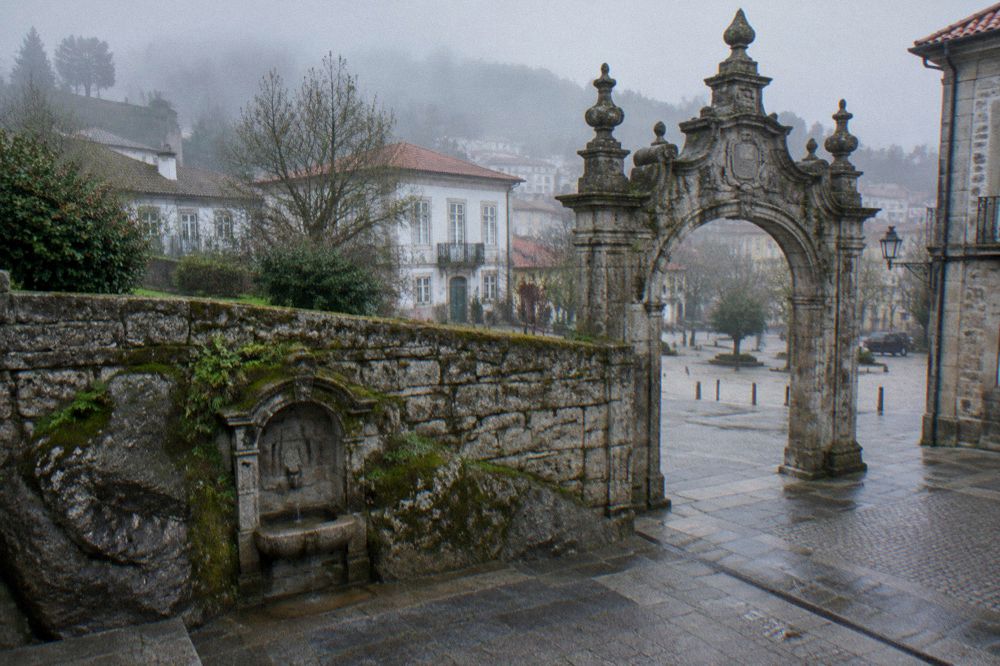 An ornate baroque archway standing at the edge of a historic Portuguese square