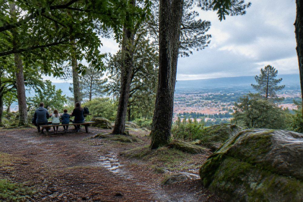 A family sitting at a wooden picnic table under trees in a hilltop park