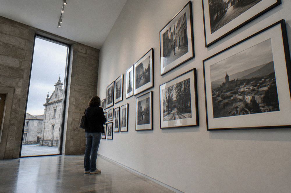 A visitor reading a wall of framed black and white photographs in a small museum gallery