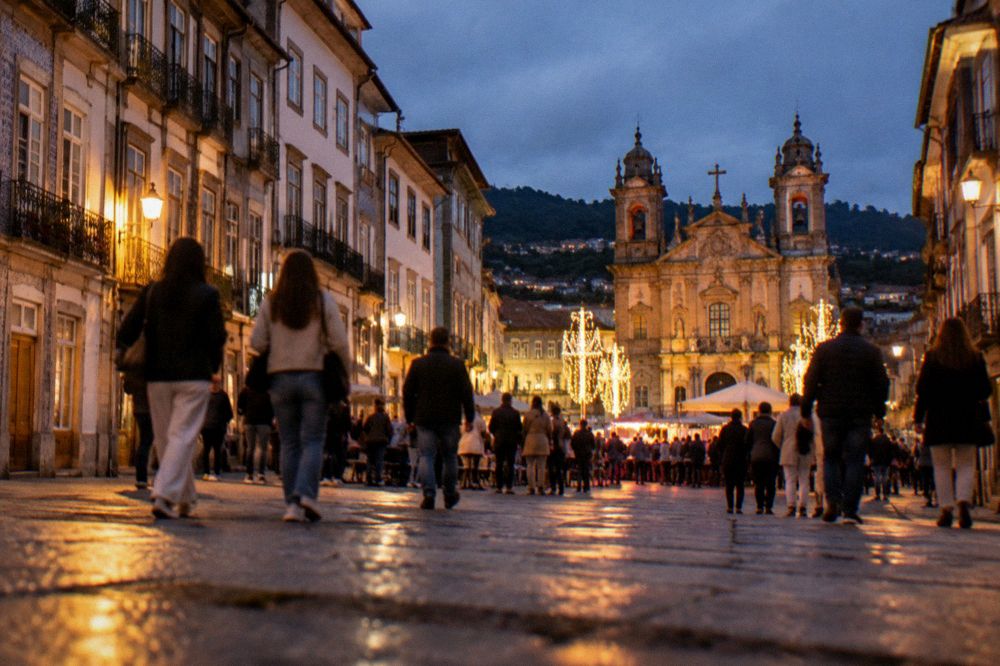 A crowd of people walking through a lit-up city square during a night festival in Braga