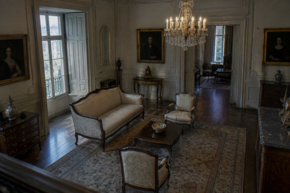 A museum interior with antique furniture, a chandelier and framed portraits on panelled walls