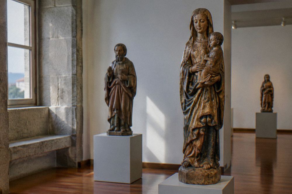 A gallery room inside the Museu Pio XII with carved wooden religious statues displayed on plinths