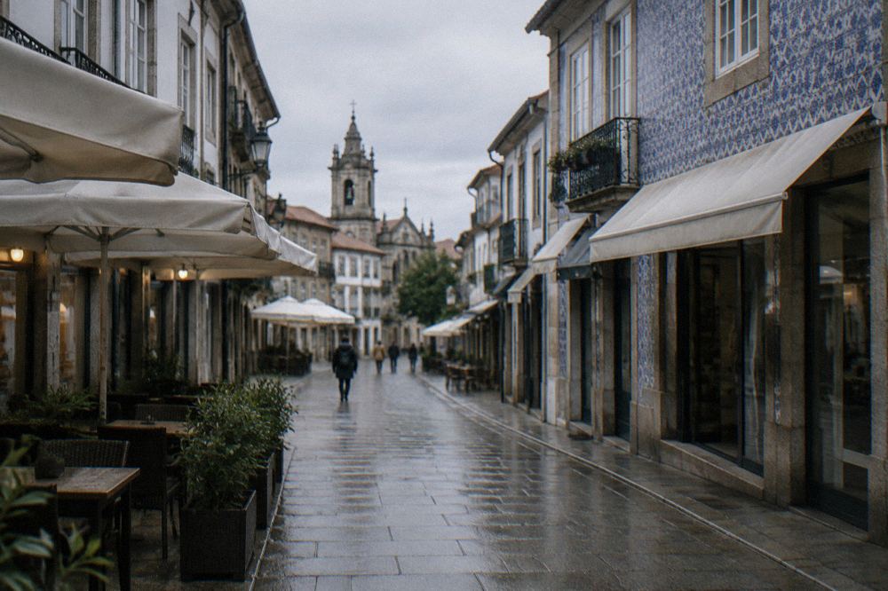 Pedestrian shopping street with granite paving and cafe awnings leading toward a church tower