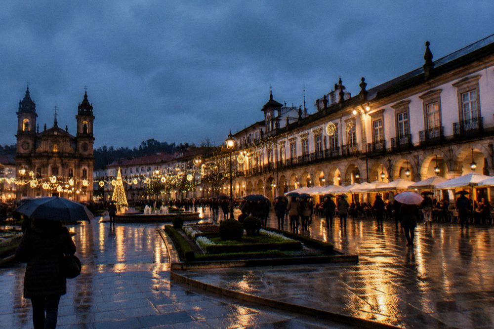 The square in December with Christmas lights strung above the terraces and a crowd at dusk