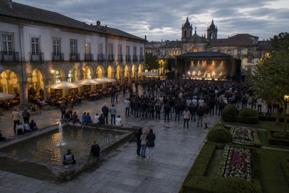 A crowd watching an evening performance on the square with stage lights and the Arcada in the background