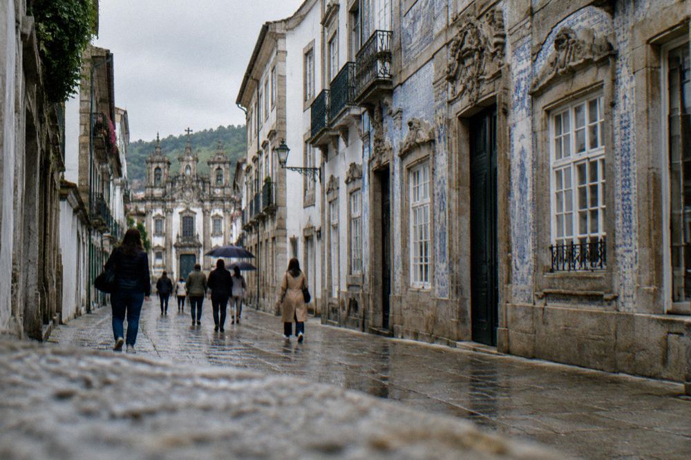 People walking past a decorated palace facade on a narrow street in Braga