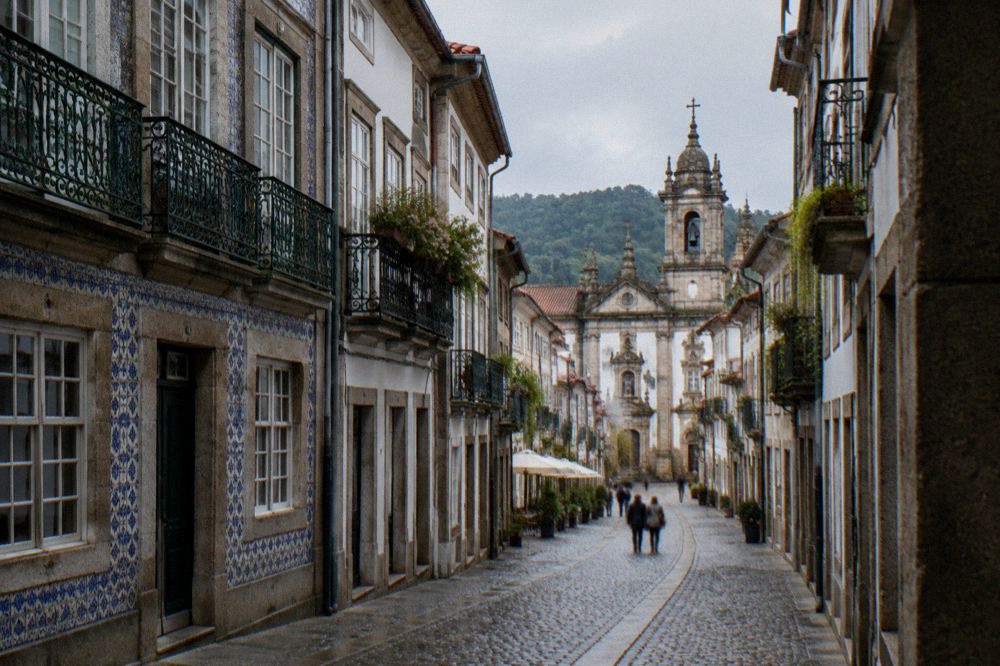 Cobblestone street with old buildings and a church tower in the background in Braga