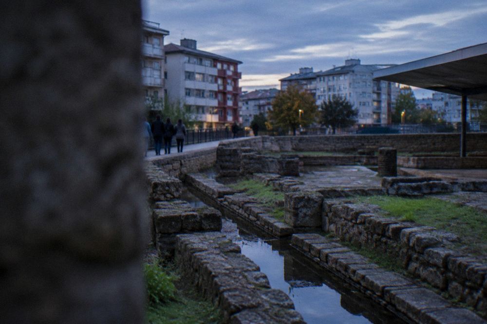 Visitors walking past excavated Roman ruins beside modern apartment buildings