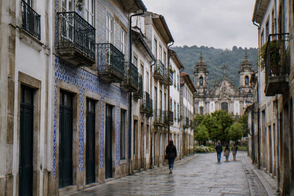 A narrow granite street in the historic centre opening toward a garden corner with trees