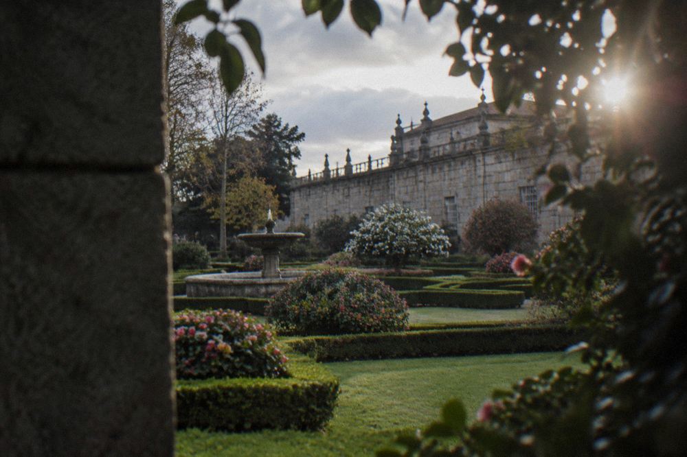 Flower beds in bloom seen from a garden corner with a granite wall and trees framing the view