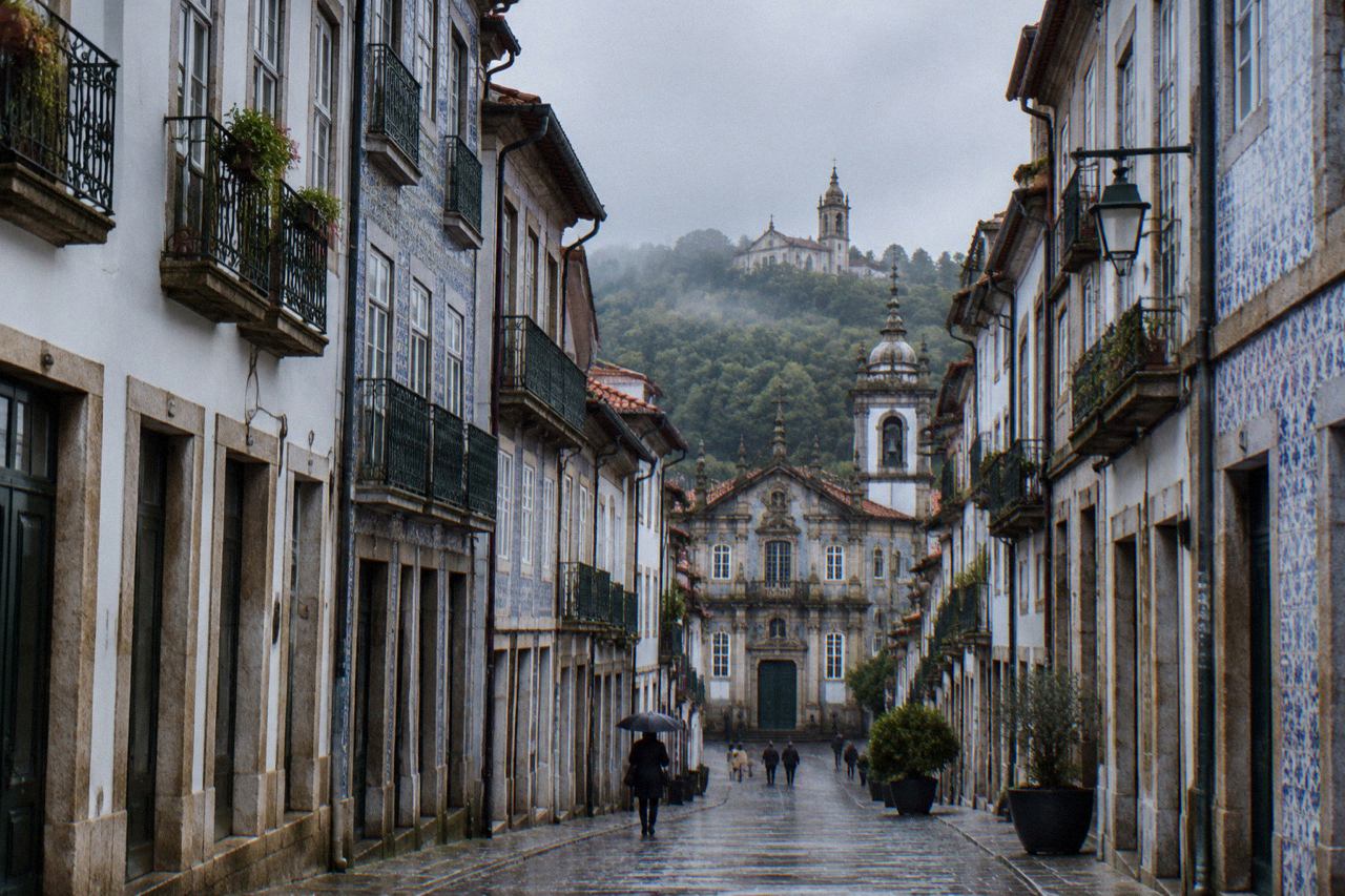 A baroque church with a single bell tower standing on a wooded hill above Braga