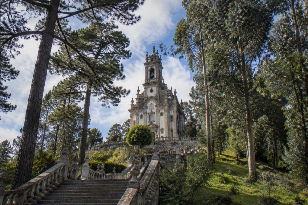 A granite baroque church tower seen through tall trees on a hillside