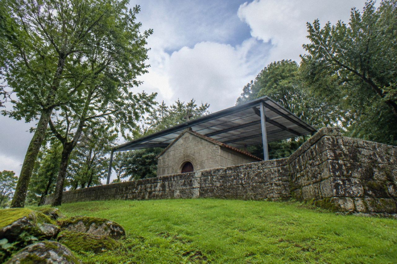 An ancient stone chapel with a simple arched doorway standing among trees on a hillside