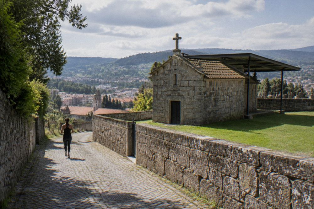 A view over rooftops and green hills from a lane beside an old chapel