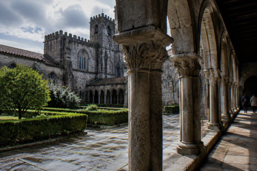 A quiet stone cloister with sunlight falling on columns and a paved walkway