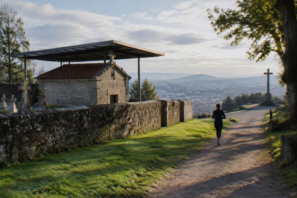 A wooded hilltop park path with a viewpoint cross above a city