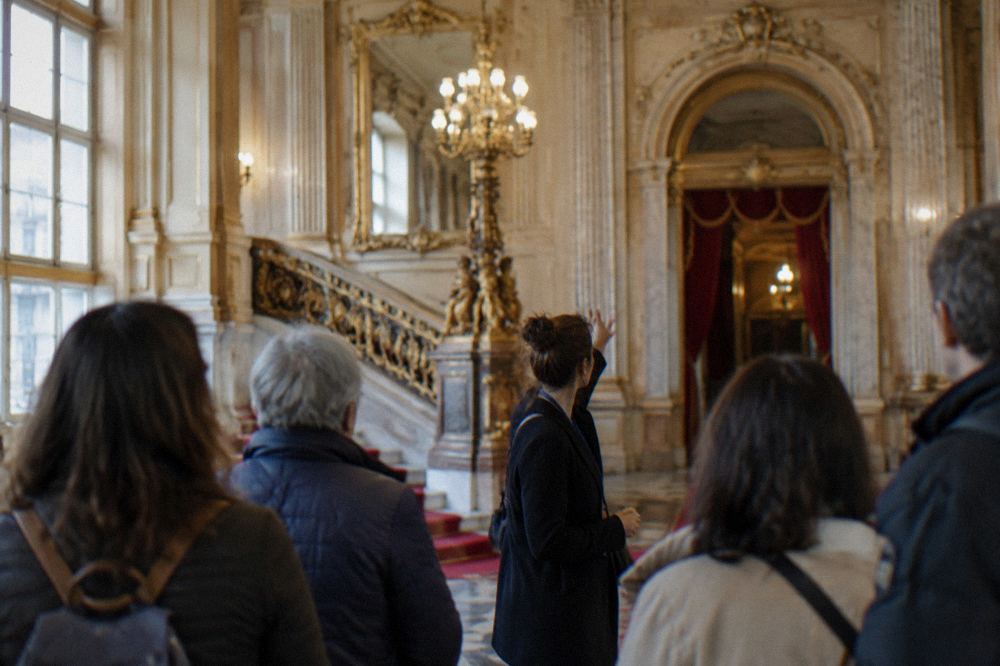 A guide leading a small group of visitors through a theatre foyer with gilded decoration