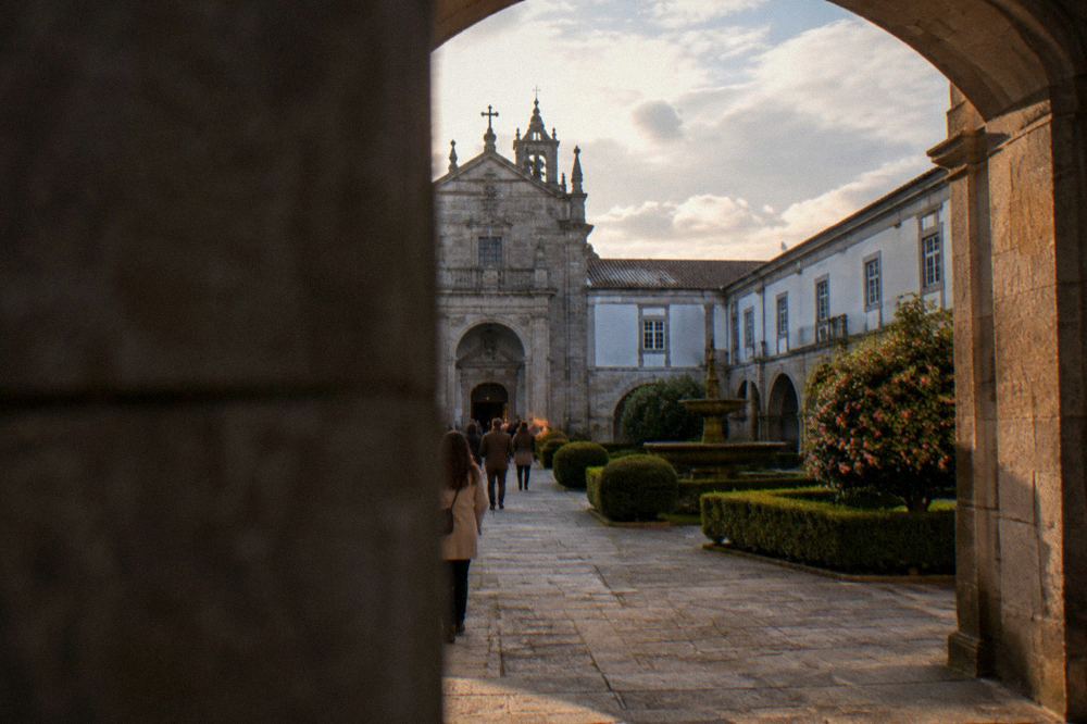 Visitors walking through a stone archway into the monastery church at Tibães