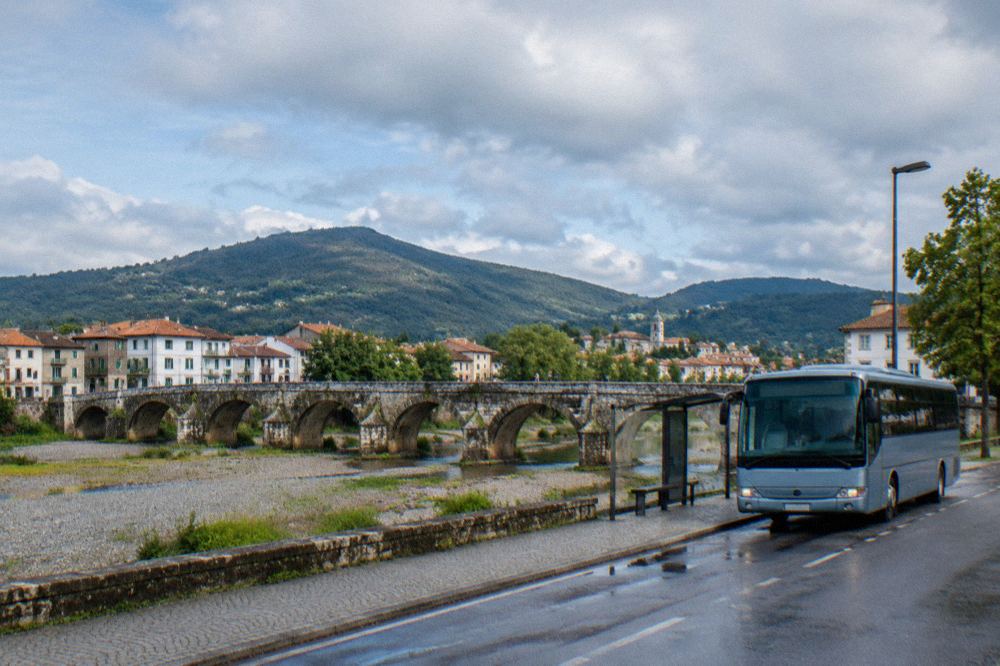 A regional bus parked at a small town station with hills in the background