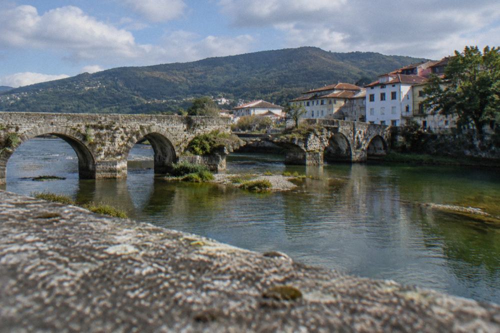 An old stone bridge with a missing arch over a green river