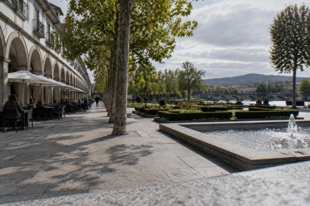 An arcaded square with plane trees and cafe tables beside a river