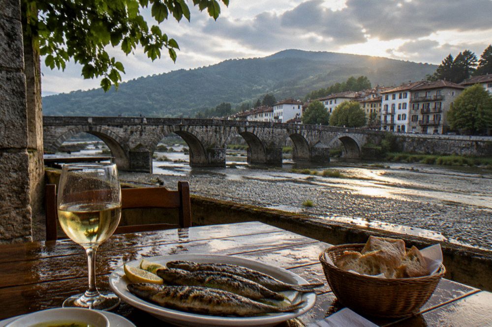 A rustic table with grilled fish, bread and a glass of white wine