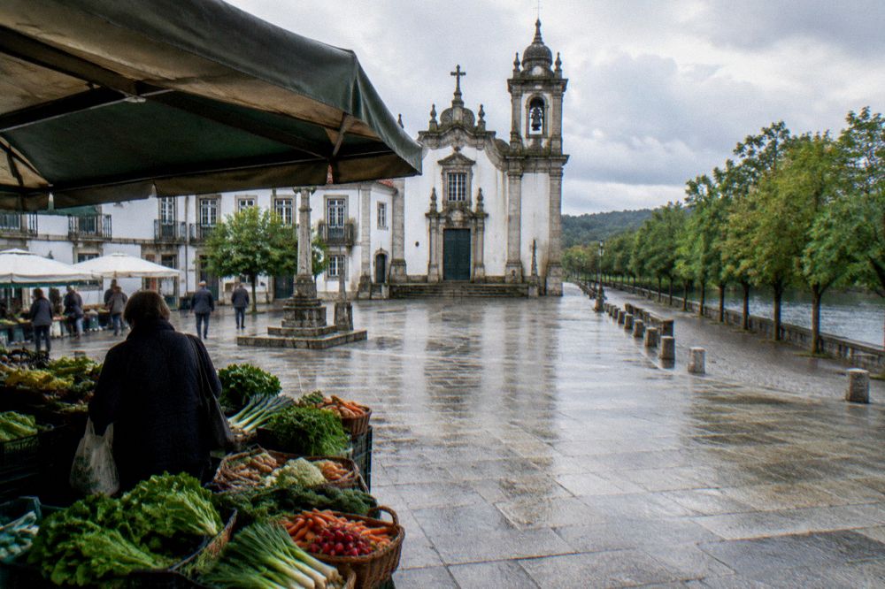 A shopper browsing a produce stall with baskets of vegetables under a market awning