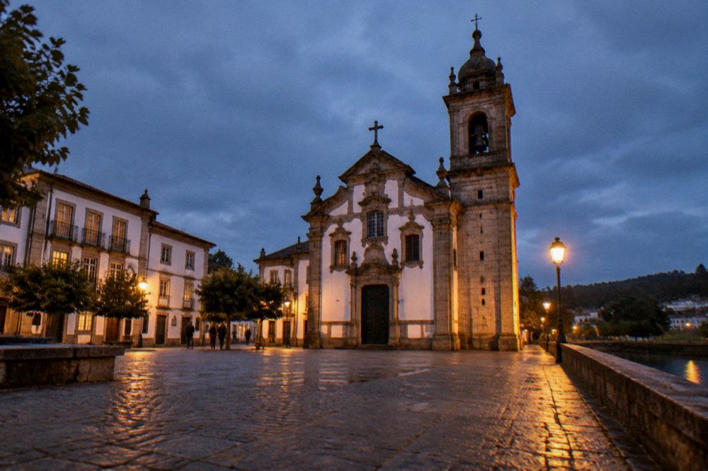 A cobbled square with historic buildings and a stone church tower in evening light in a northern Portuguese town
