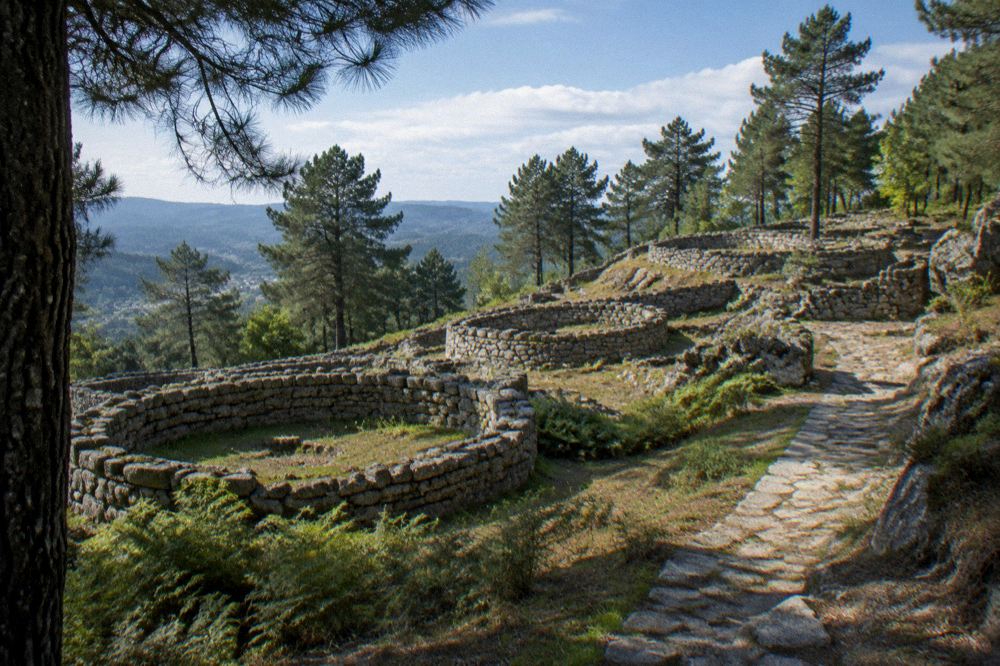 Wide view of the hillfort's stone walls and house footings under a clear sky