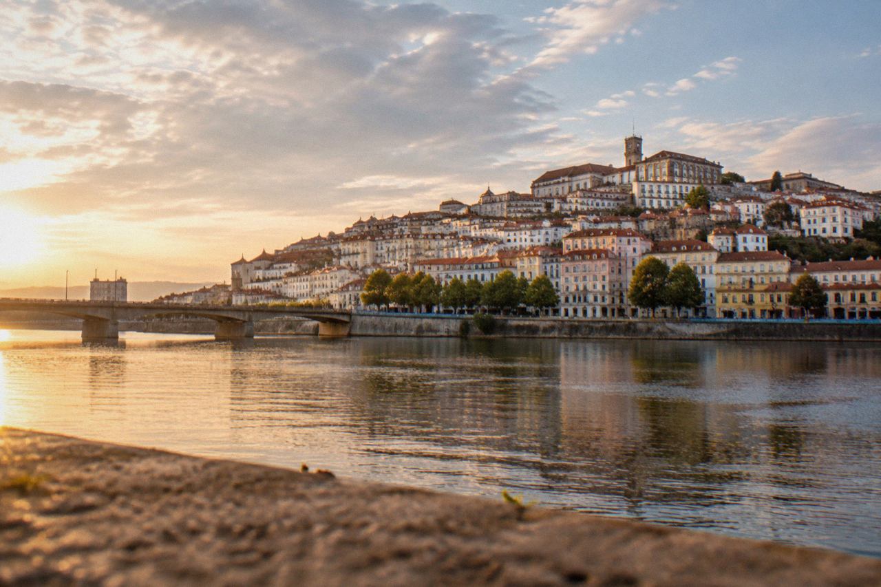 The old university buildings of Coimbra rising above the Mondego river, seen from the opposite bank on a clear afternoon