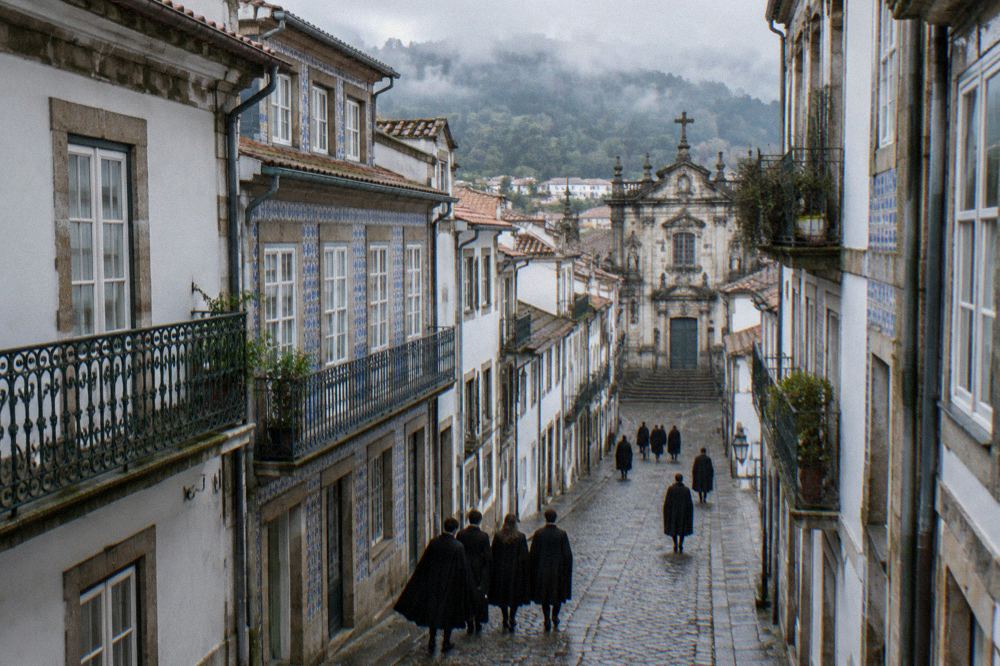 Students in black capes walking through a narrow cobblestone street in Coimbra's old town